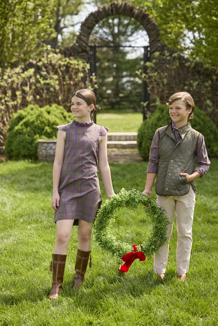 Little English traditional children's clothing. Olive and maroon Thornhill Plaid column dress with capped sleeves, ruffled neckline, and fixed bow in back for older girls for the holidays.  Boys Button Down Shirt in Thornhill Plaid with Classic Quilted Vest in Olive layered over top. Paired with Classic Pant in tan Stone Corduroy.