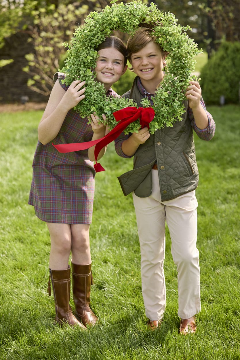 Little English traditional children's clothing. Olive and maroon Thornhill Plaid column dress with capped sleeves, ruffled neckline, and fixed bow in back for older girls for the holidays.  Boys Button Down Shirt in Thornhill Plaid with Classic Quilted Vest in Olive layered over top. Paired with Classic Pant in tan Stone Corduroy.