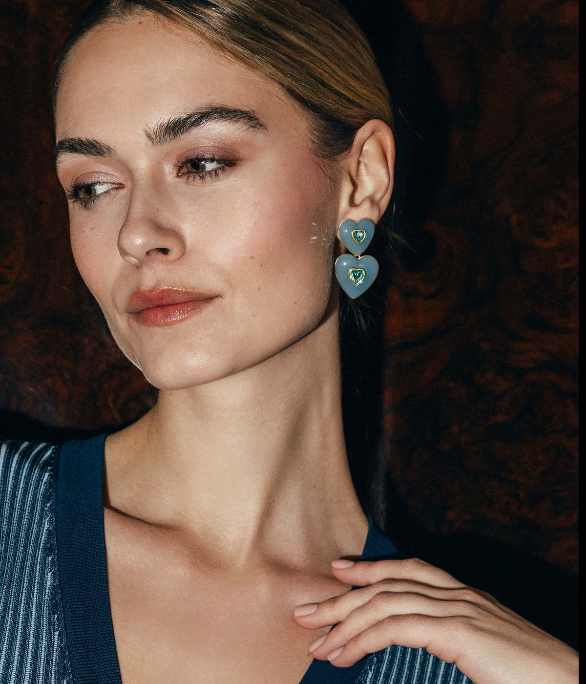 Close-up of Elodie Heart Drop Earrings worn by model showing double blue resin hearts with crystal centers on dark background