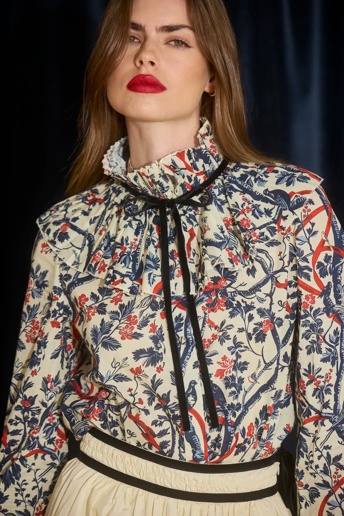 The Eloise Blouse is framed by a pleated yoke, a high ruffled collar, and tied with velvet ribbon. 