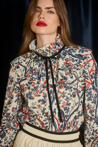 The Eloise Blouse is framed by a pleated yoke, a high ruffled collar, and tied with velvet ribbon. 