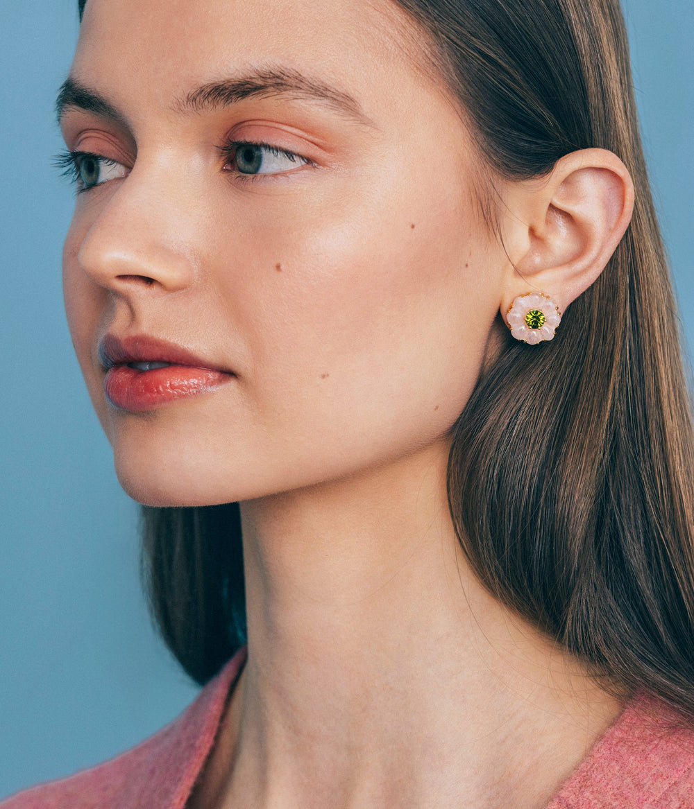 Close-up side view of Emeline flower stud earrings in rose quartz with green crystal center against blue background