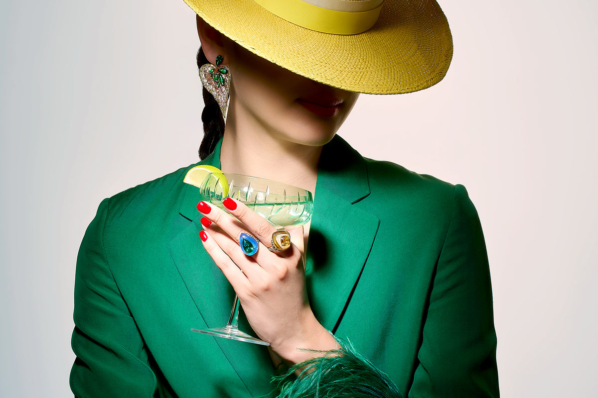 Close-up of Emerald Beetroot Begonia earrings worn by model showcasing green gems and leaf motif, blazer and yellow hat