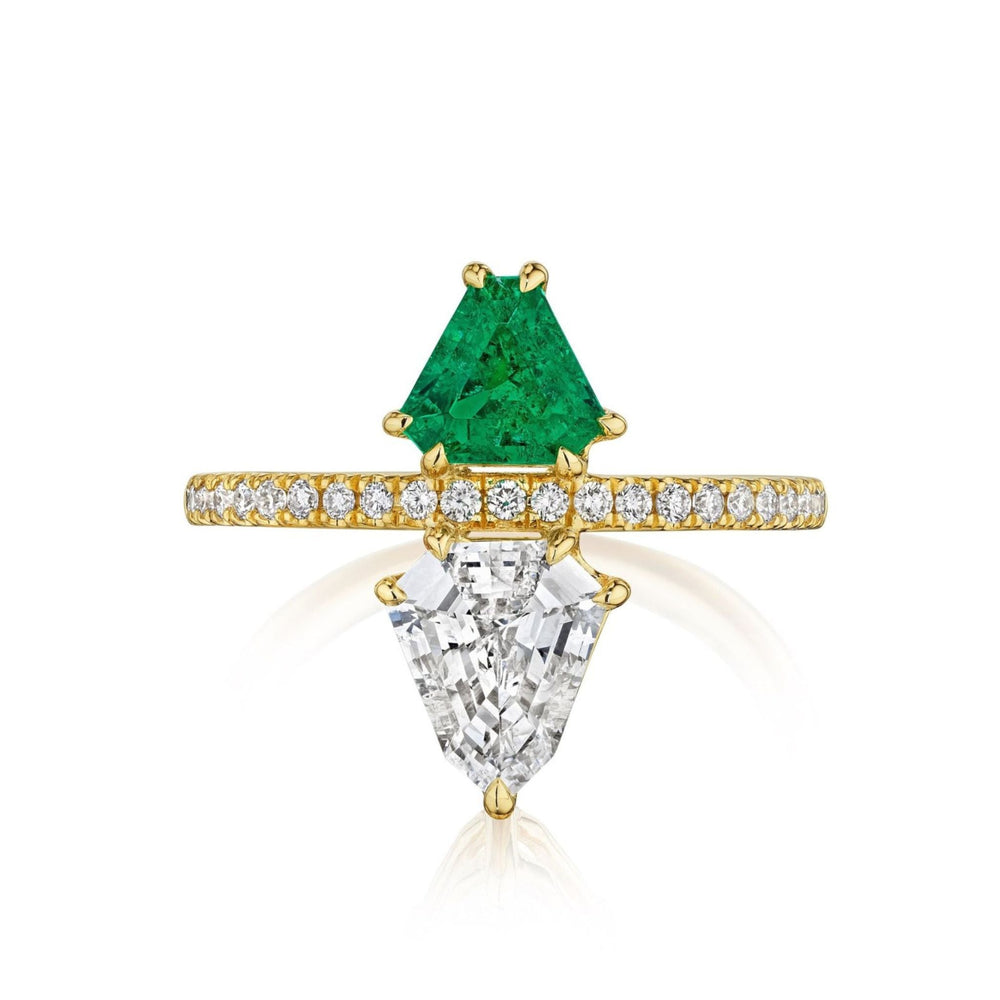 The Emerald and Diamond Double Shield Ring in Yellow Gold showcases a triangular green emerald and a trapezoid white diamond, separated by a yellow gold band adorned with small round diamonds.