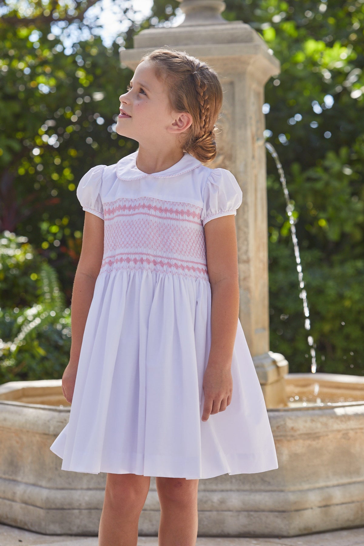 Three-quarter view of Smocked Emery Dress in Light Pink showing smocked bodice, Peter Pan collar, cap sleeves and skirt