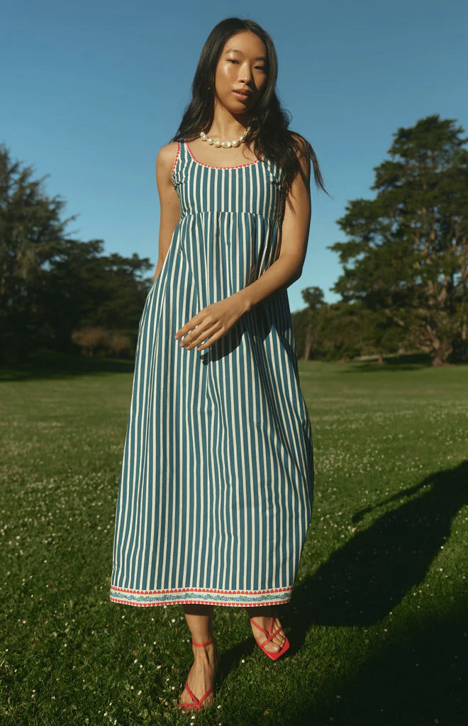 Front view of Emily Dress in Navy Stripe showcasing coastal blue and white stripes with red hem details on a model in a grassy park