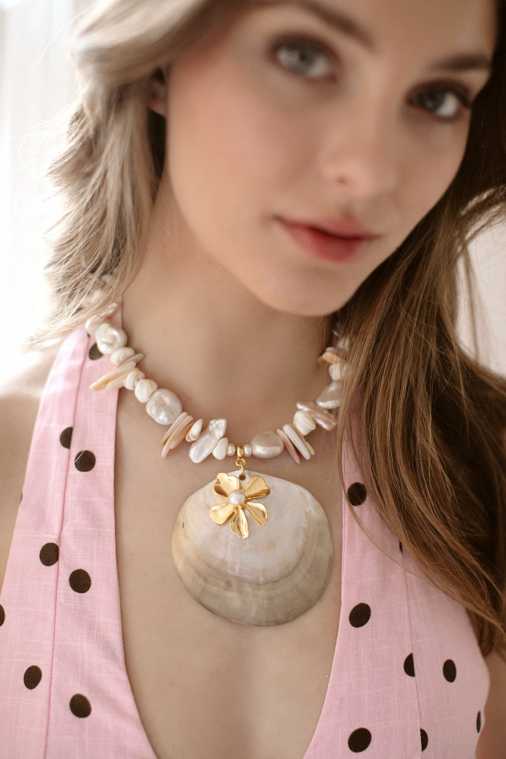 Close-up of Emme Necklace on model showcasing a large Tahitian oyster shell pendant with 24k gold-plated flower and a strand of shell sticks and freshwater pearls