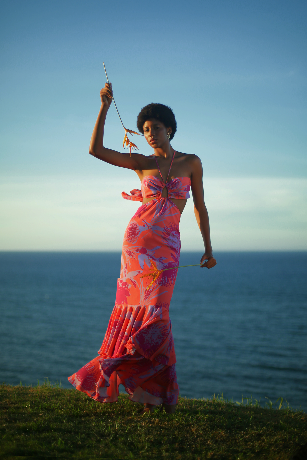 Front of Espuma De Mar coral-print maxi dress showcasing halter tie, front cutout, fitted bodice and ruffle hem by the sea