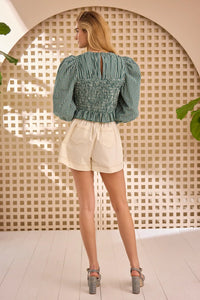 The Eubanks Top has a fitted bodice, puff sleeves, smocked cuffs, shirred yoke, and purl edge trim.