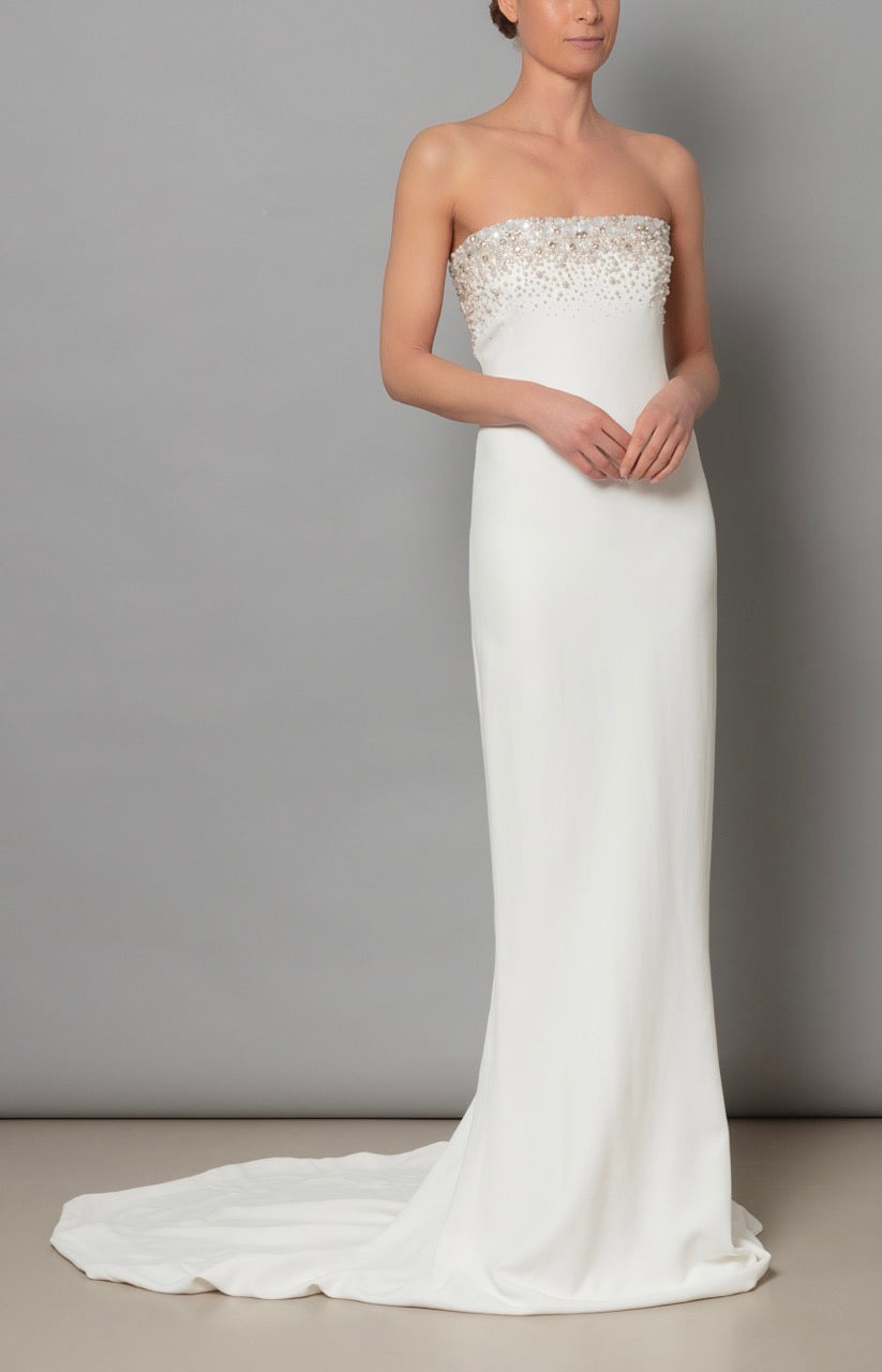 Front view of Eve dress in ivory showcasing strapless beaded bodice, slim crepe skirt and train on gray background
