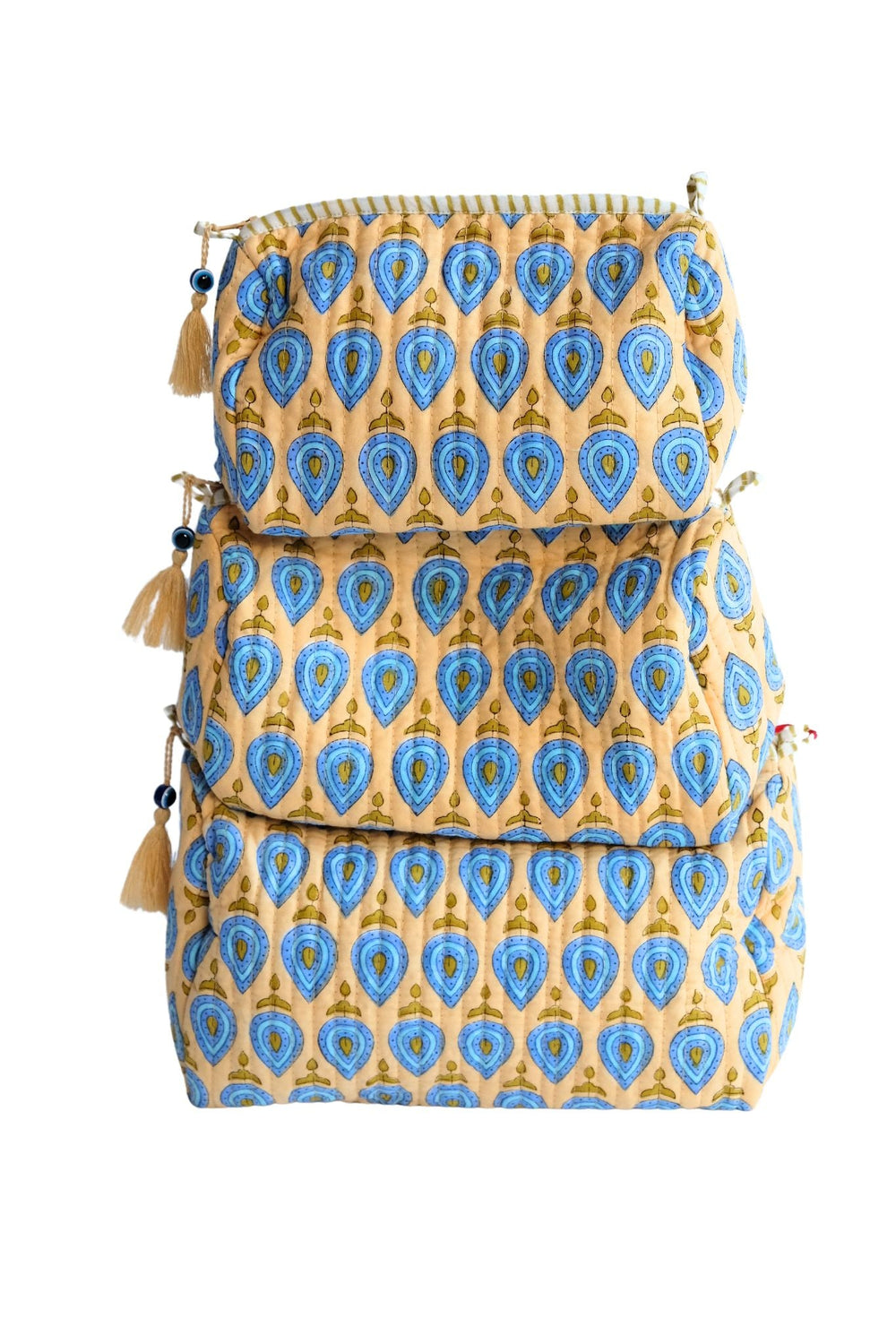 Front view of three stacked Evil Eye Charm toiletry bags showcasing blue evil-eye block-print pattern, tassel zipper charms, and quilted quilted cotton on white background