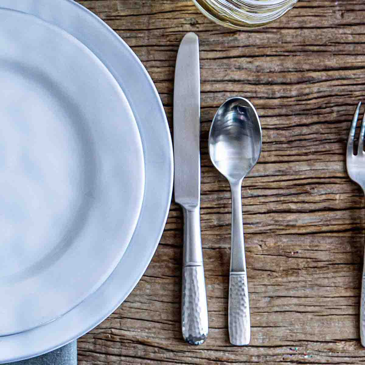 Close-up of Carine 20-Piece Place Setting in Bright Satin showcasing contrasting textured handles on a wooden table