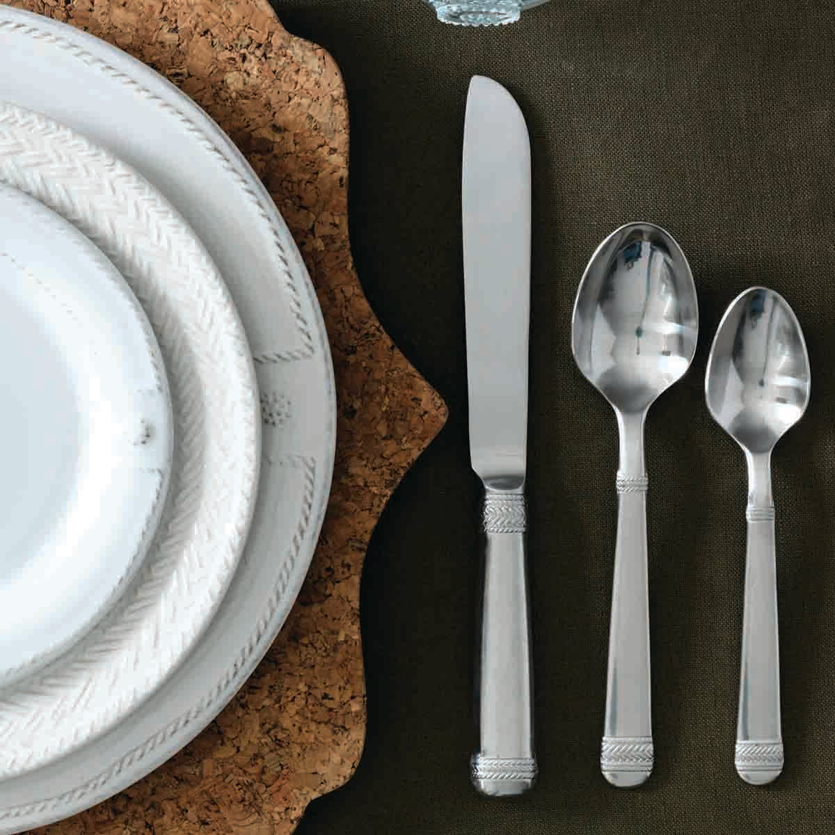 Close view of Le Panier 20 Piece Place Setting in Bright Satin showcasing braided handles with white plates on a cork placemat