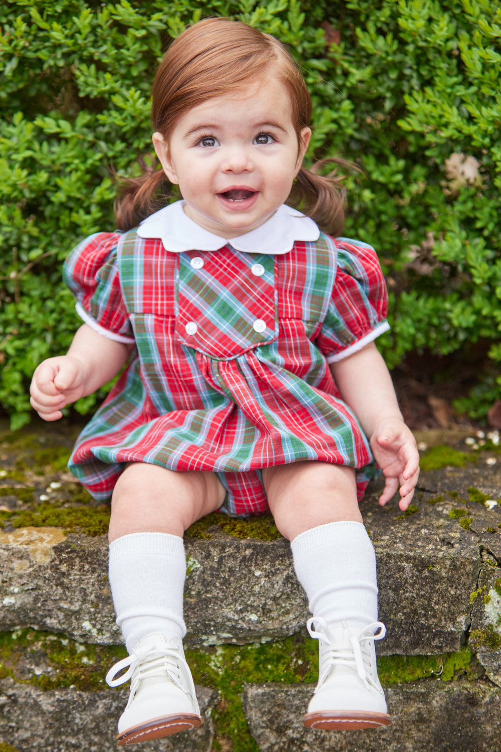 Front view of Fallon Bubble in Highlands Tartan on toddler showing red-green plaid, white collar and puff sleeves on stone ledge