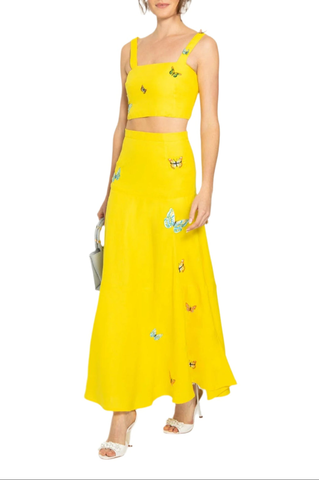 Three-quarter front of Derin skirt set in bright yellow on model showcasing high-waist A-line skirt and cropped square-neck top with butterfly embroidery on white background