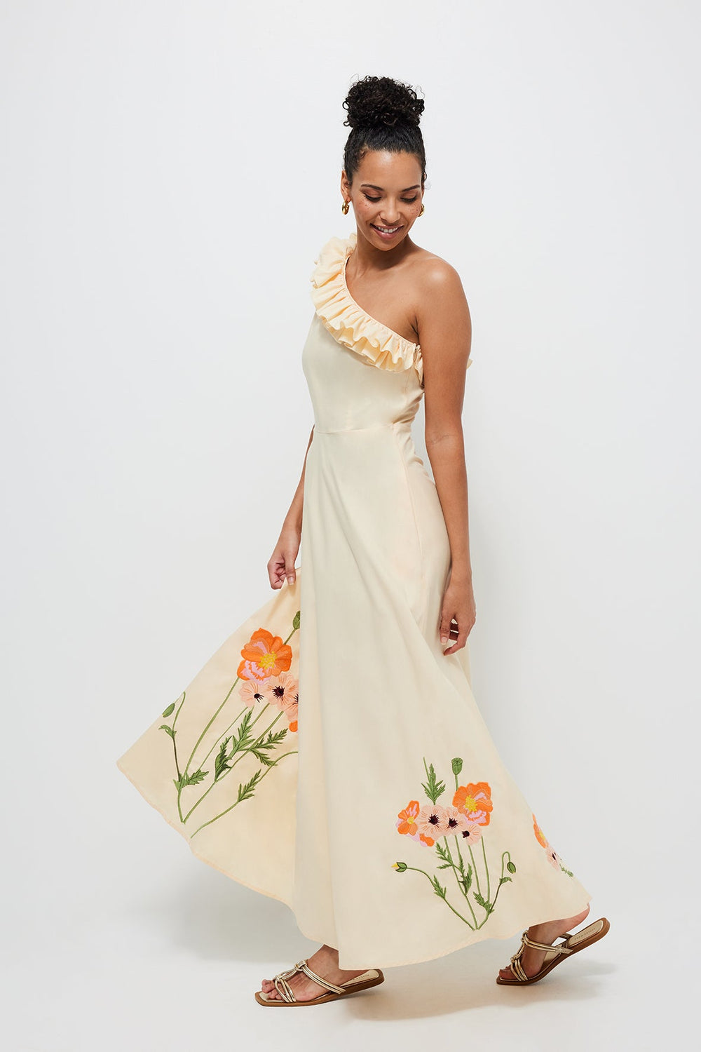 Side view of Melisa Dress with one-shoulder ruffle neckline and orange floral embroidery on cream fabric against white background