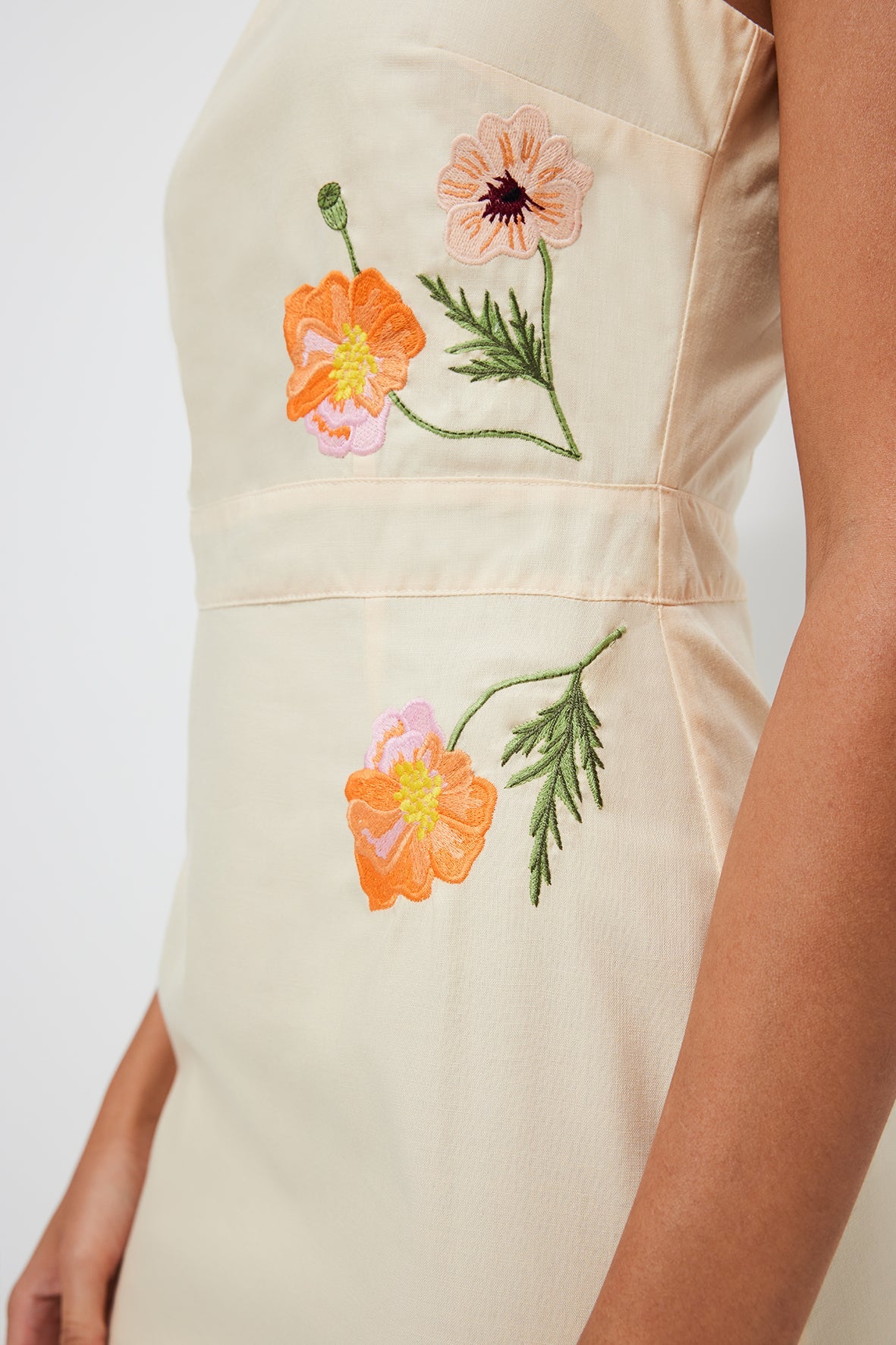 Close up of Zennur Dress showcasing orange and pink floral embroidery at the waist on light yellow fabric
