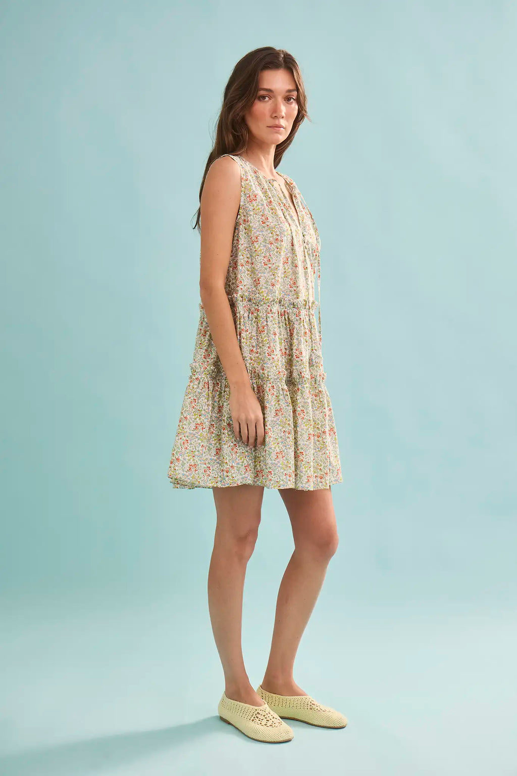 The Fawn Dress in Coral Multi paired with pale yellow shoes on a blue background.