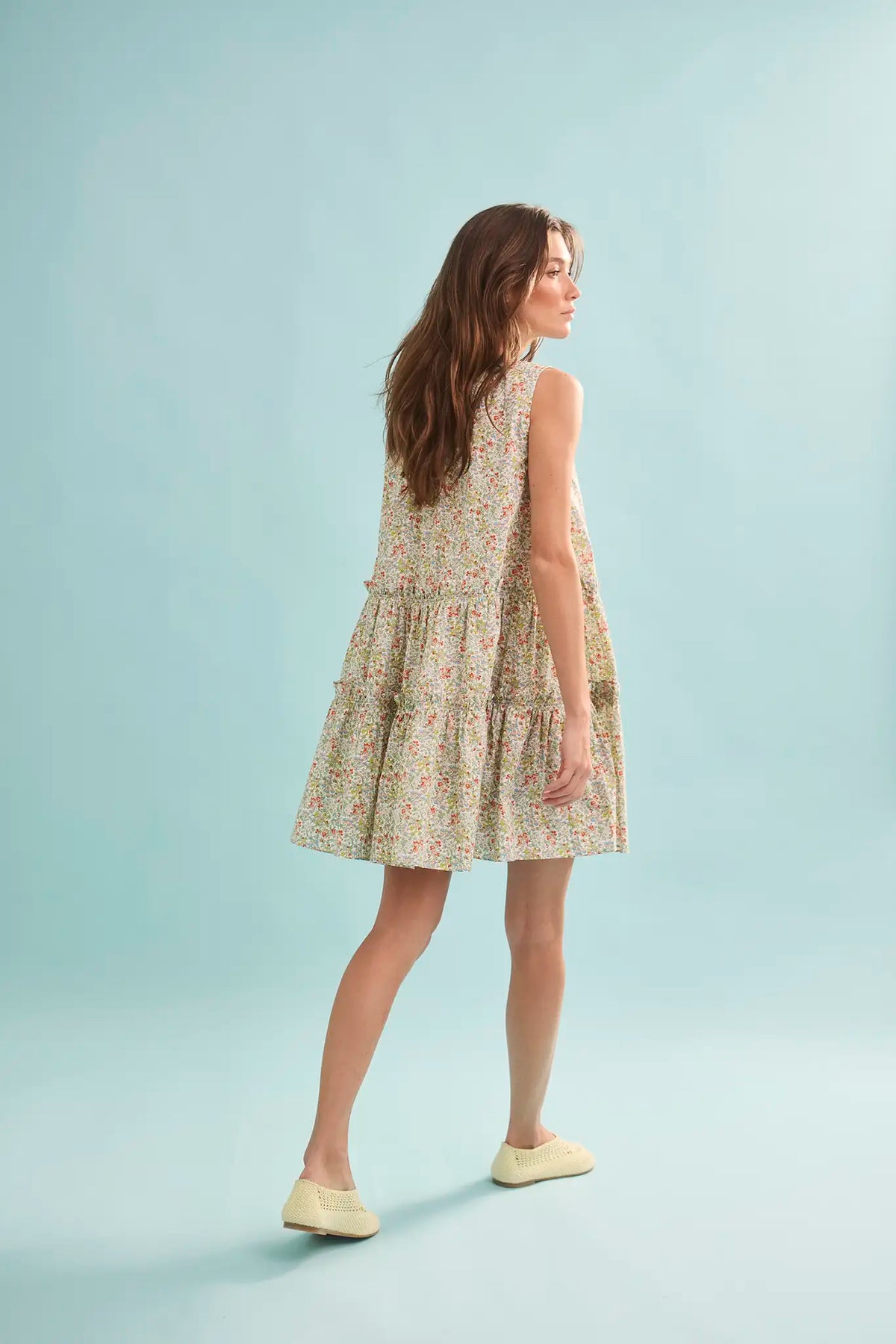 The Fawn Dress in Coral Multi paired with pale yellow shoes on a blue background.