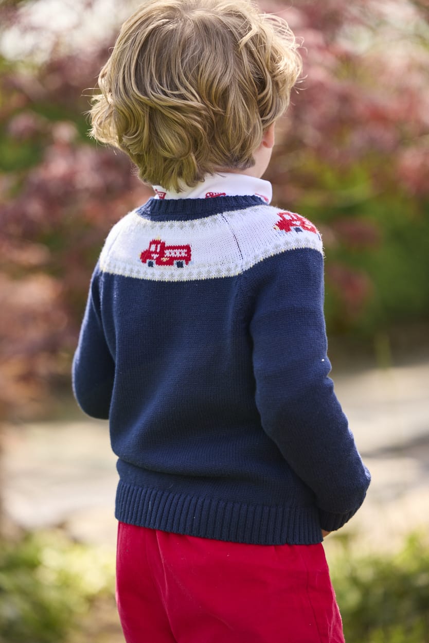 Little English traditional children's clothing. Navy crew neck sweater with red fire truck fair isle detail. Layered over white knit turtleneck with all-over fire truck print. Paired with red corduroy banded pants.  Fall outfit for toddler boys.
