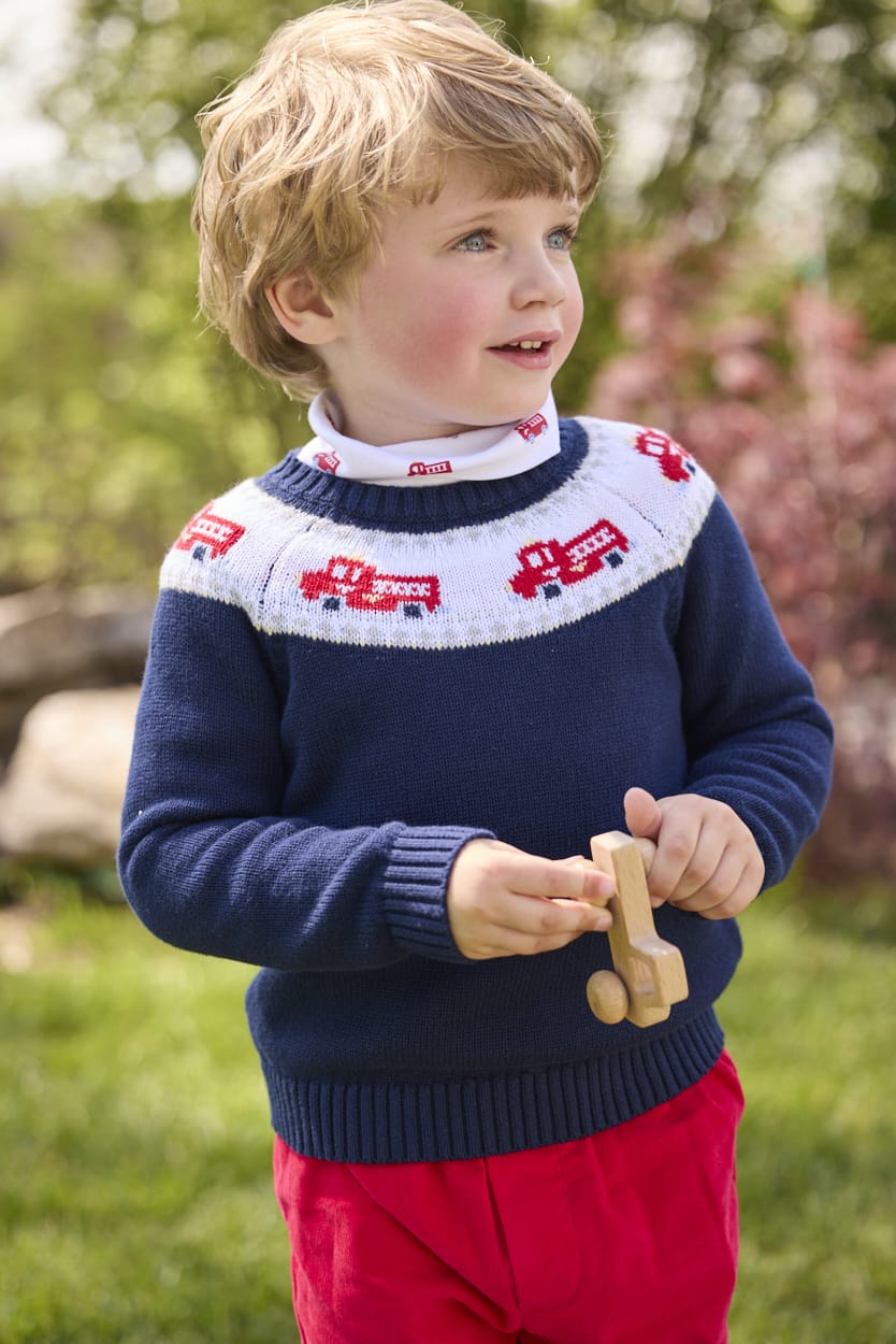 Little English traditional children's clothing. Navy crew neck sweater with red fire truck fair isle detail. Layered over white knit turtleneck with all-over fire truck print. Paired with red corduroy banded pants.  Fall outfit for toddler boys.
