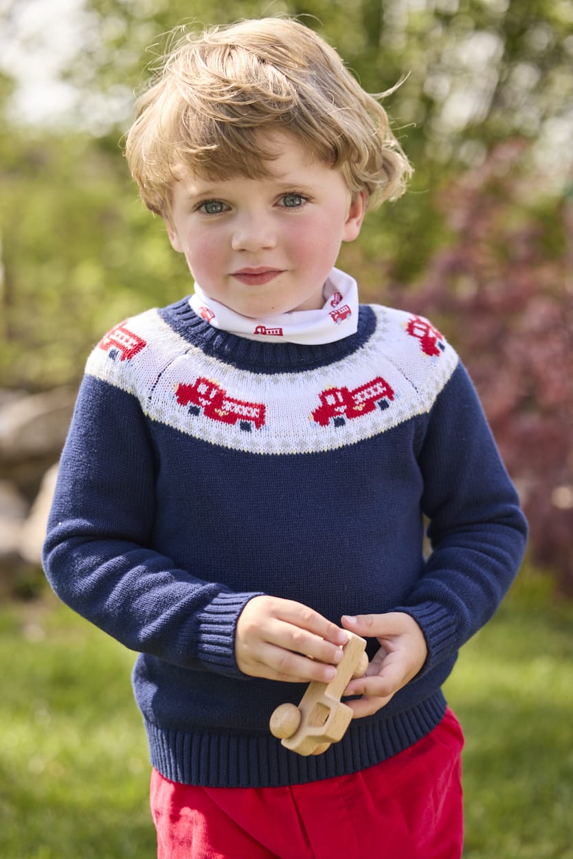 Little English traditional children's clothing. Navy crew neck sweater with red fire truck fair isle detail. Layered over white knit turtleneck with all-over fire truck print. Paired with red corduroy banded pants.  Fall outfit for toddler boys.