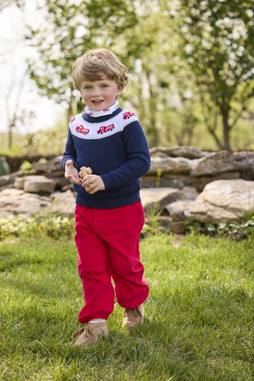 Little English traditional children's clothing. Navy crew neck sweater with red fire truck fair isle detail. Layered over white knit turtleneck with all-over fire truck print. Paired with red corduroy banded pants.  Fall outfit for toddler boys.