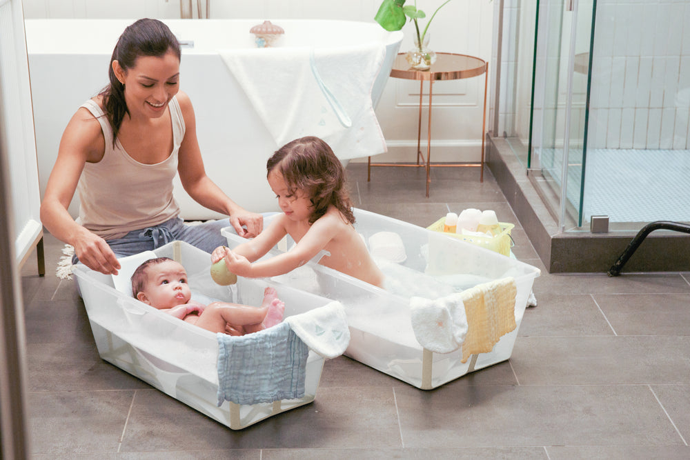 Mother bathing a baby and a toddler in two Sandy beige Flexi Bath tubs on a bathroom floor