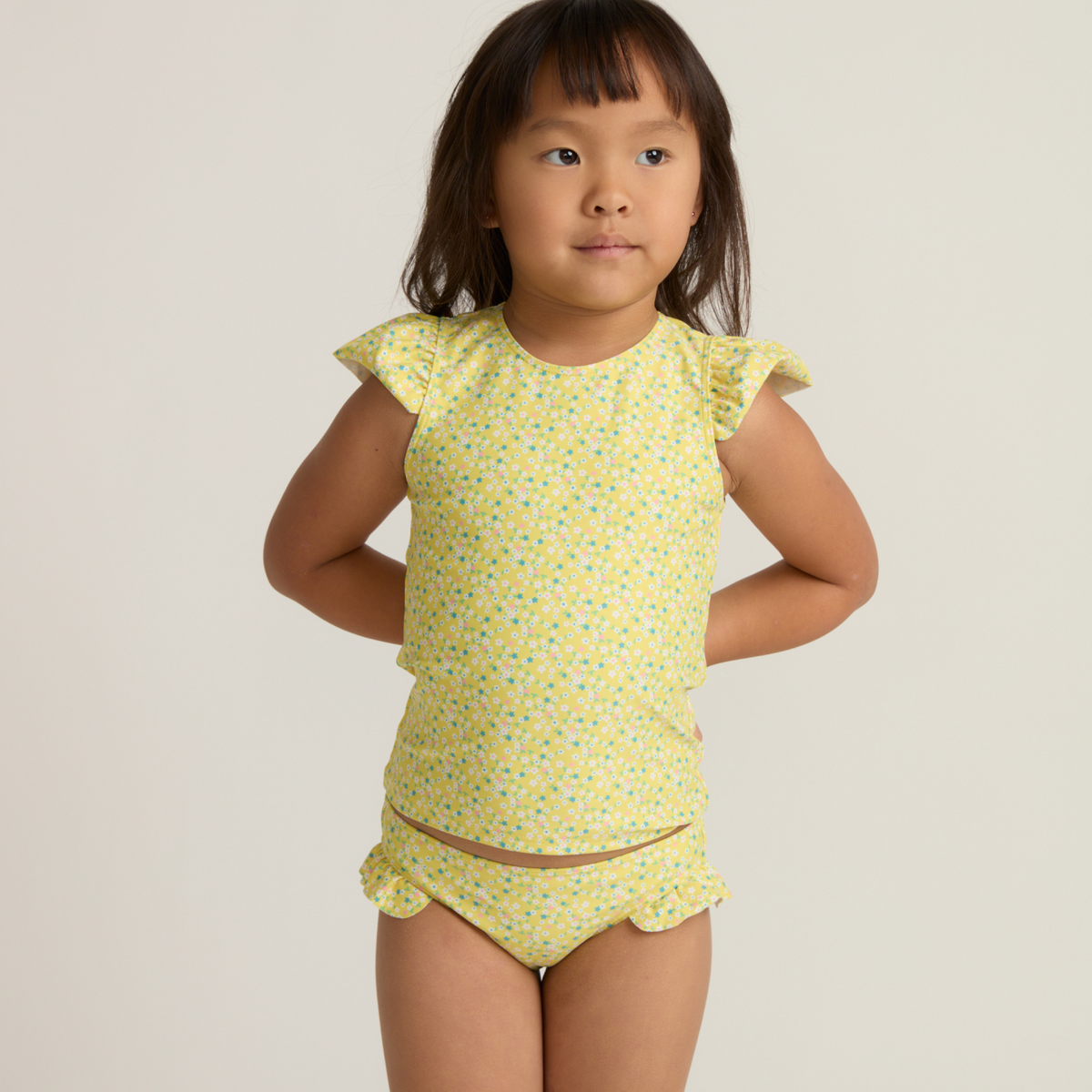 Front view of yellow Petite Fleur cap sleeve rashguard and matching ruffle bottoms on child model against light background