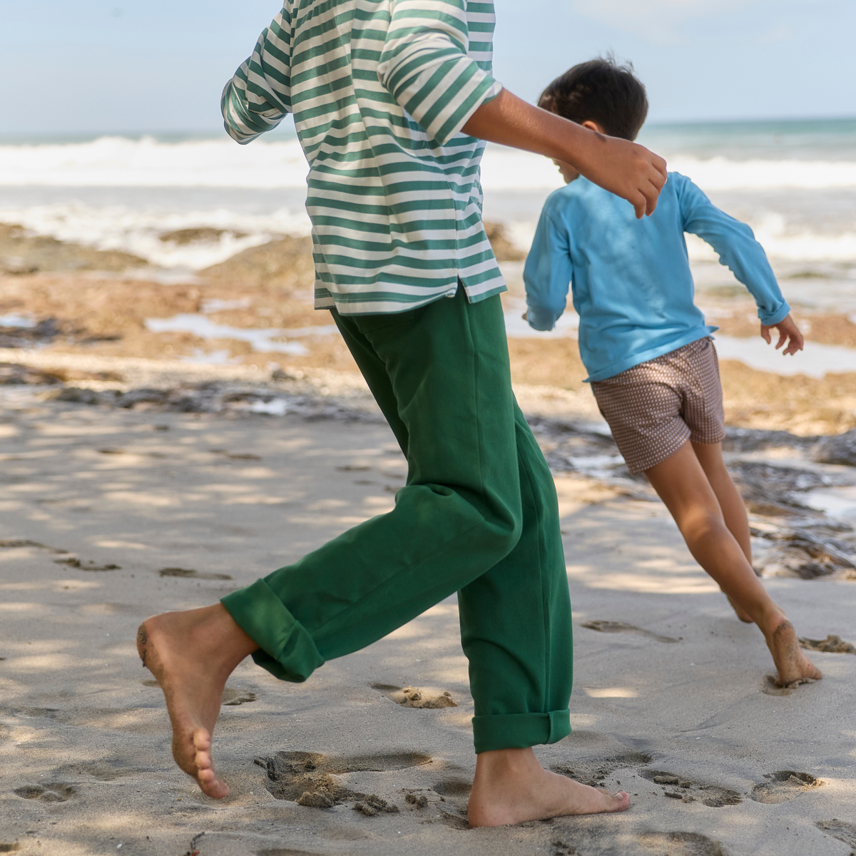 People running barefoot along a beach, with green twill pants visible on the adult
