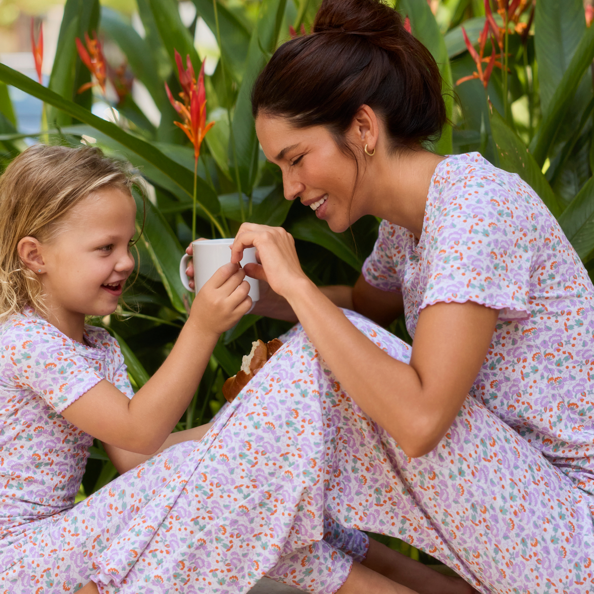 Woman and child in matching orchid floral pajamas smiling together among tropical plants