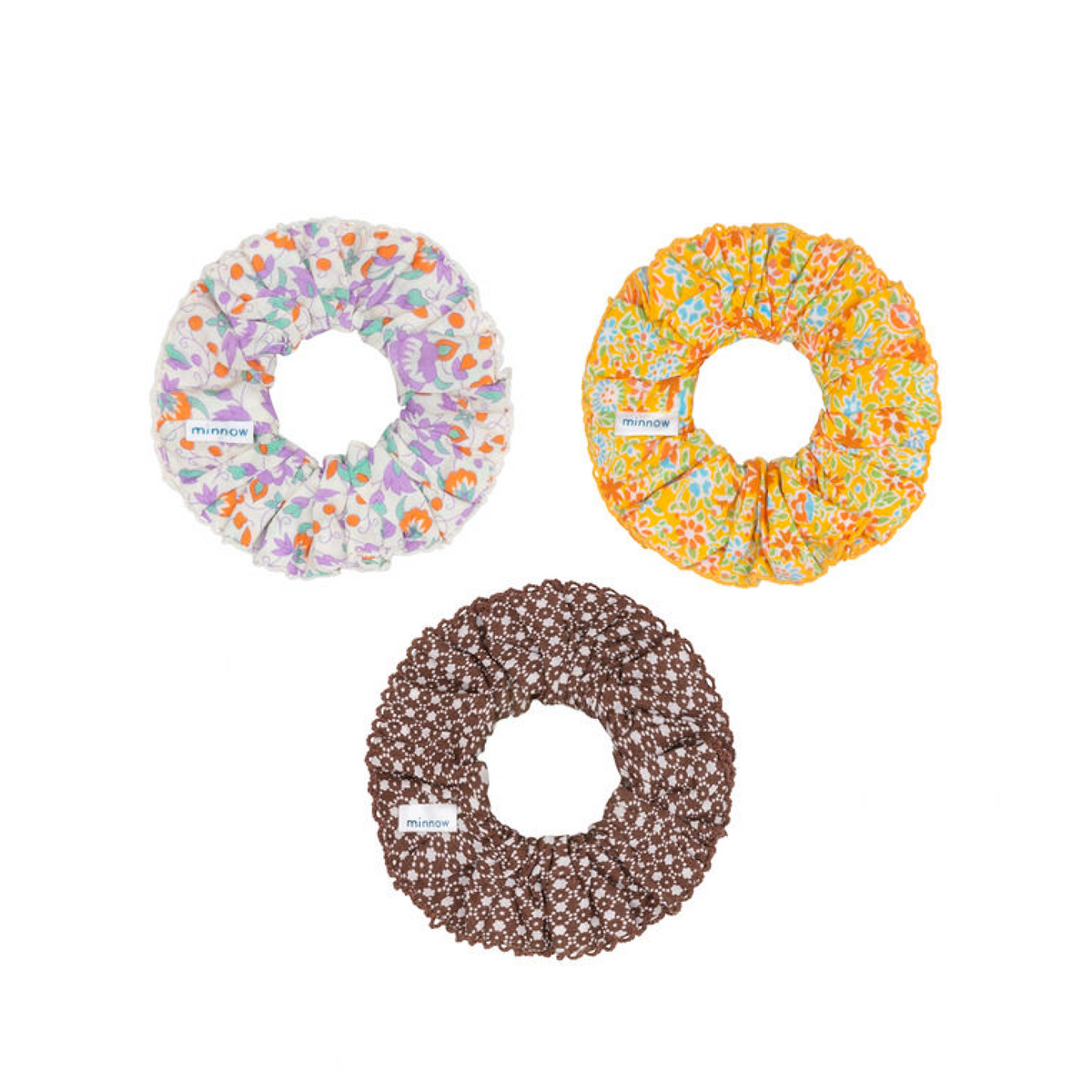 Top view of three cotton scrunchies showcasing orchid floral, marigold floral, and café flora prints with picot trim on white background