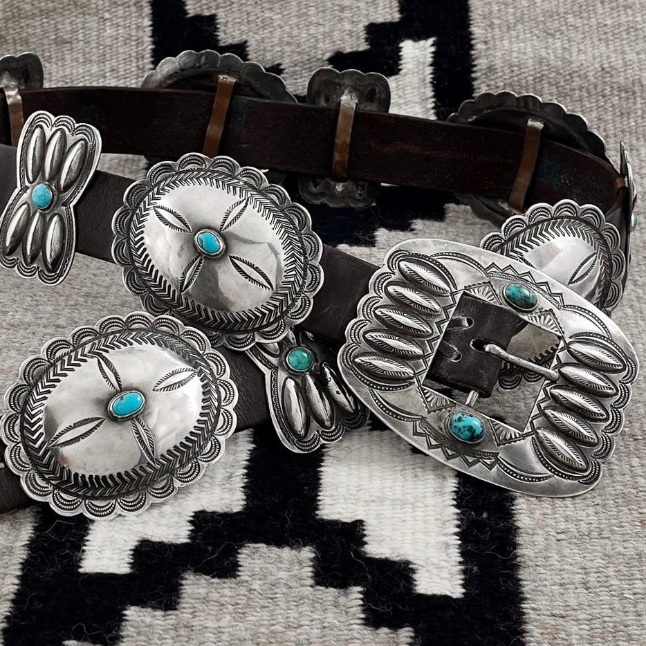 Close-up of vintage concho belt showcasing sterling silver conchos, American turquoise, and butterfly details on a patterned textile