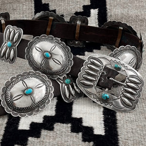 Close-up of vintage concho belt showcasing sterling silver conchos, American turquoise, and butterfly details on a patterned textile