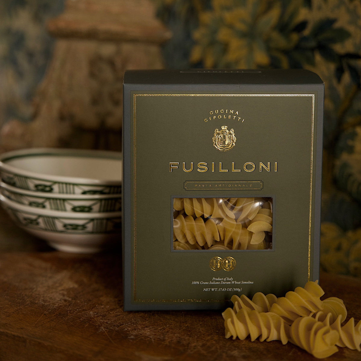 Box of Cucina Cipoletti Fusilloni pasta with a clear window showing spiral pasta, styled on a wooden surface with ceramic bowls in the background.