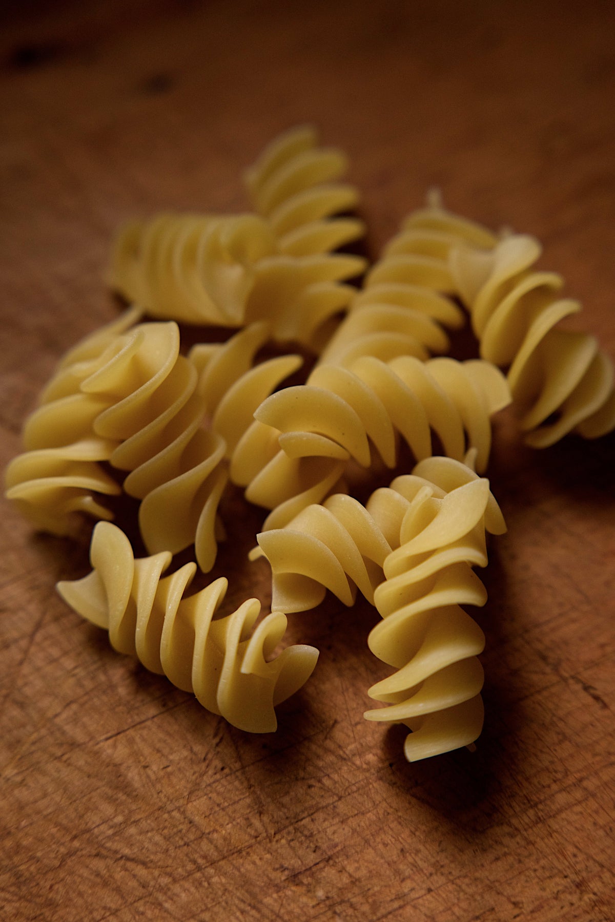 Close-up of uncooked Fusilloni pasta pieces on a wooden surface, showing their spiral shape and rough texture.