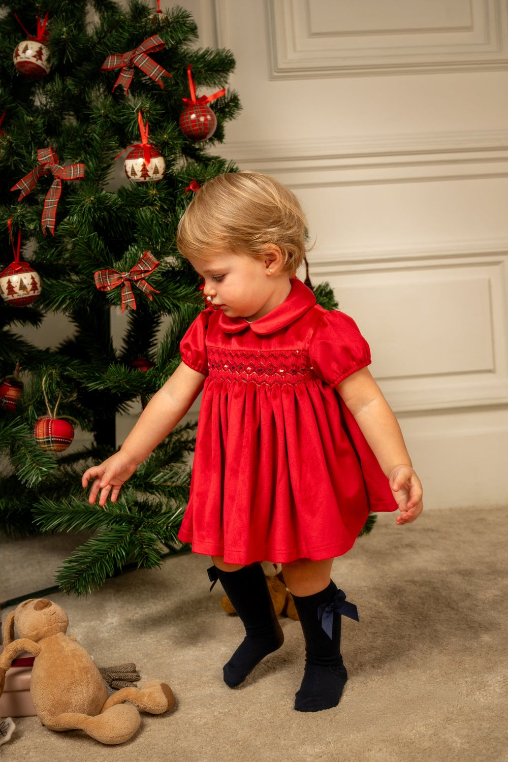 Front view of Camille velvet short dress in cherry on toddler, showing smocked bodice and Peter Pan collar, tree background