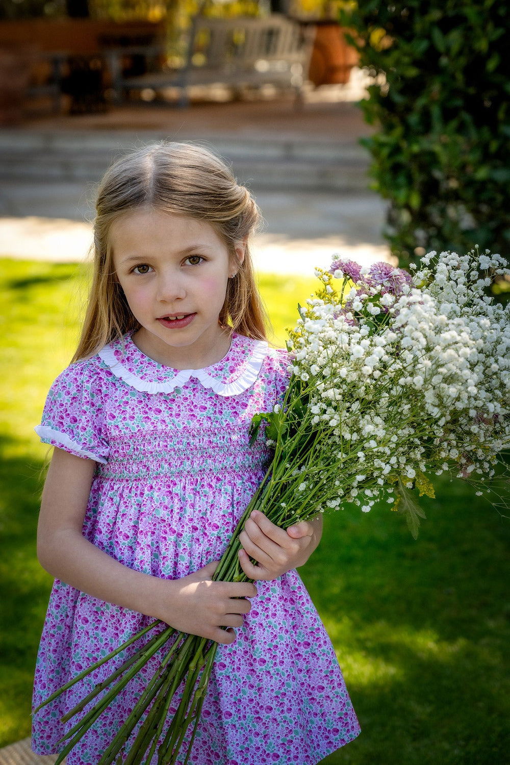 Front view of Olivia Dress in Radiant Poppies showing smocked bodice, Peter Pan collar and short sleeves on child outdoors