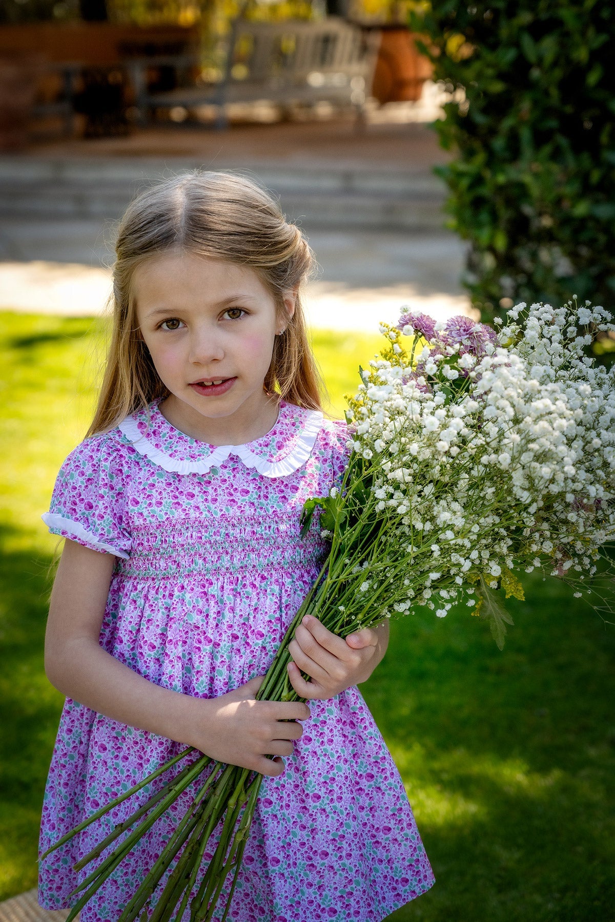 Front view of Olivia Dress in Radiant Poppies showing smocked bodice, Peter Pan collar and short sleeves on child outdoors