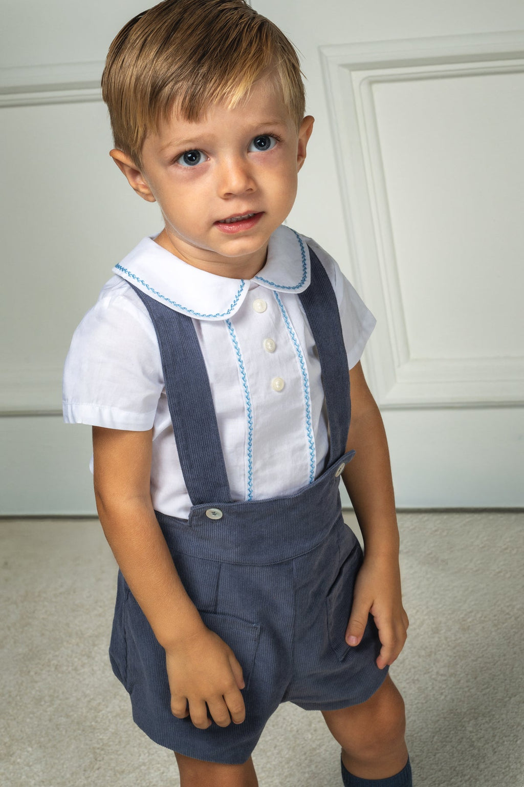 Front view of Eduardo Shirt in Bluebell showcasing Peter Pan collar, short sleeves, and herringbone embroidery on a child indoors