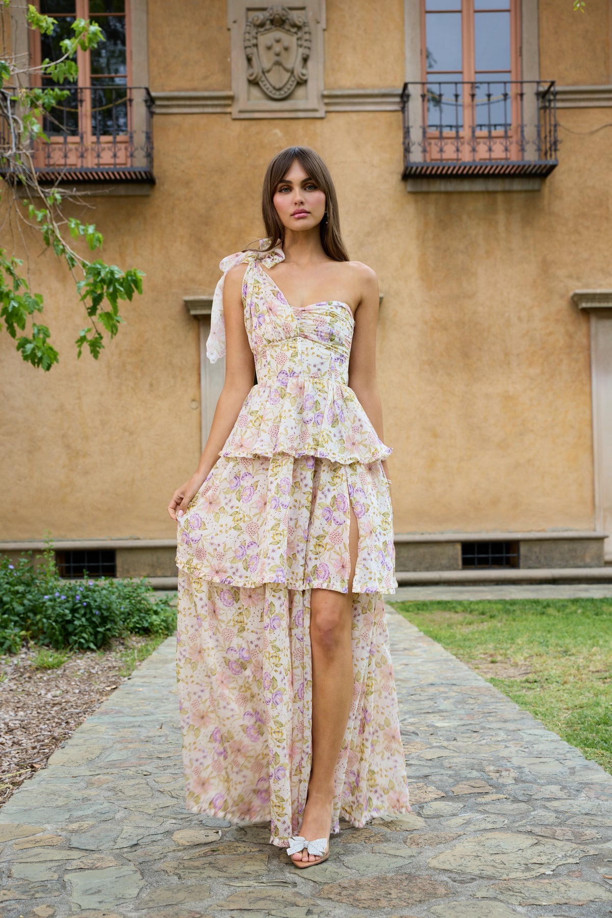 Front view of The Grace Dress in Cordoba print on a model, showing one-shoulder tie, ruched bodice and tiered high-low skirt with thigh slit