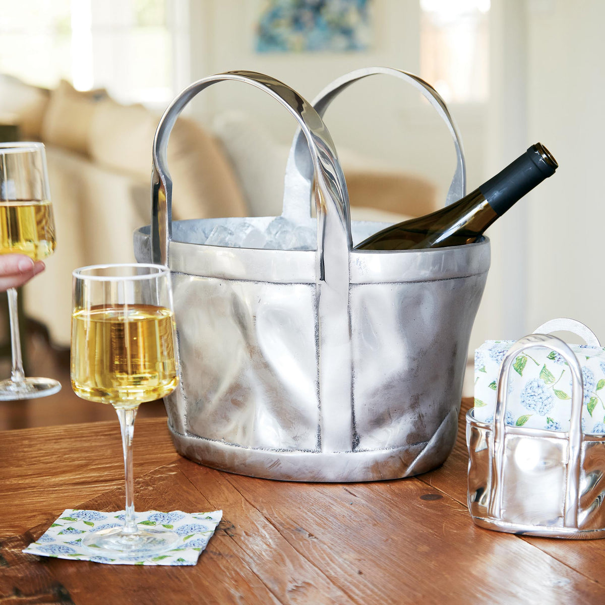 Three-quarter view of Tote Bag Wine Bucket showing sculpted metallic tote holding a wine bottle in ice on a wood table