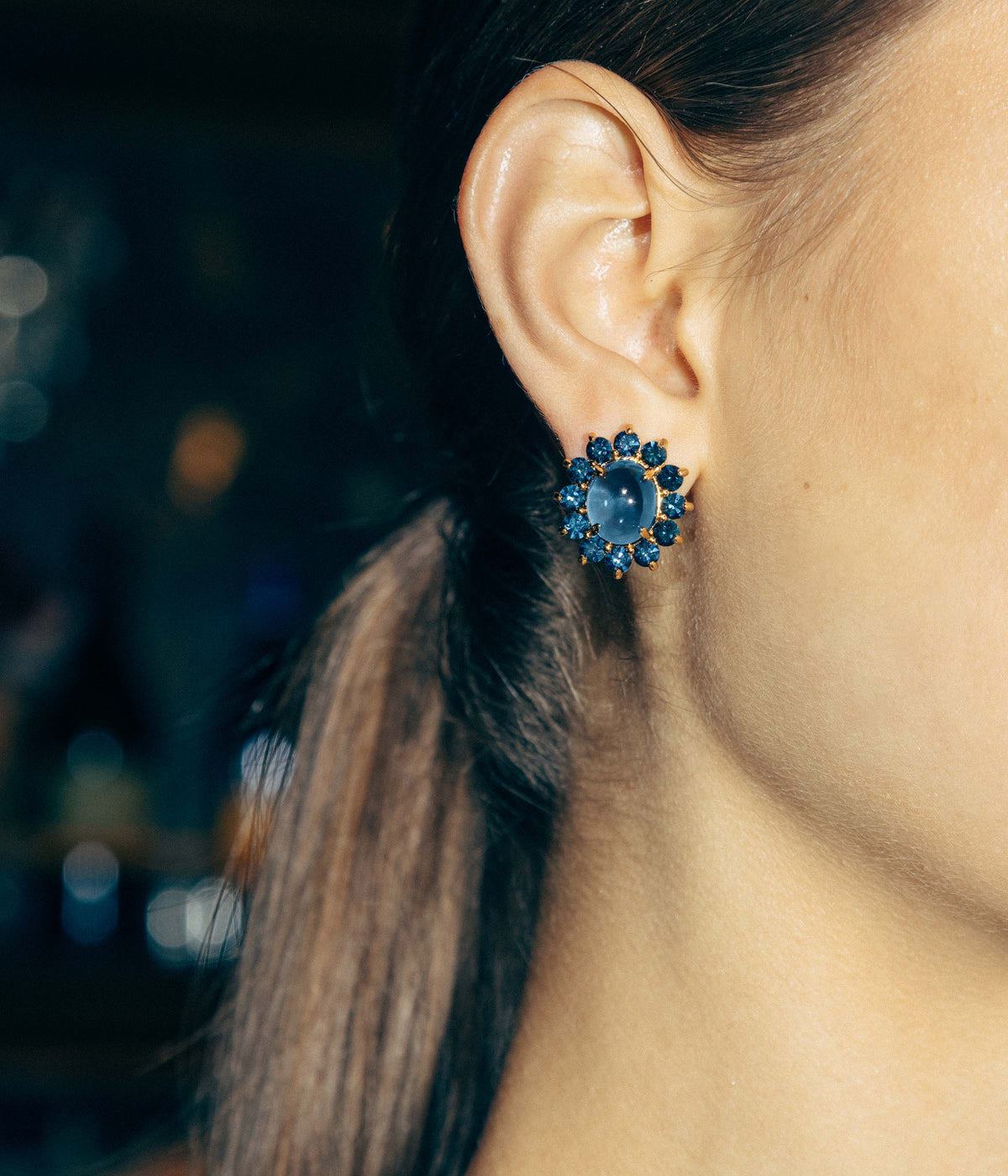Close-up of Georgie Stud Earrings in Navy showcasing a smooth cabochon and crystal halo on an ear with dark hair background