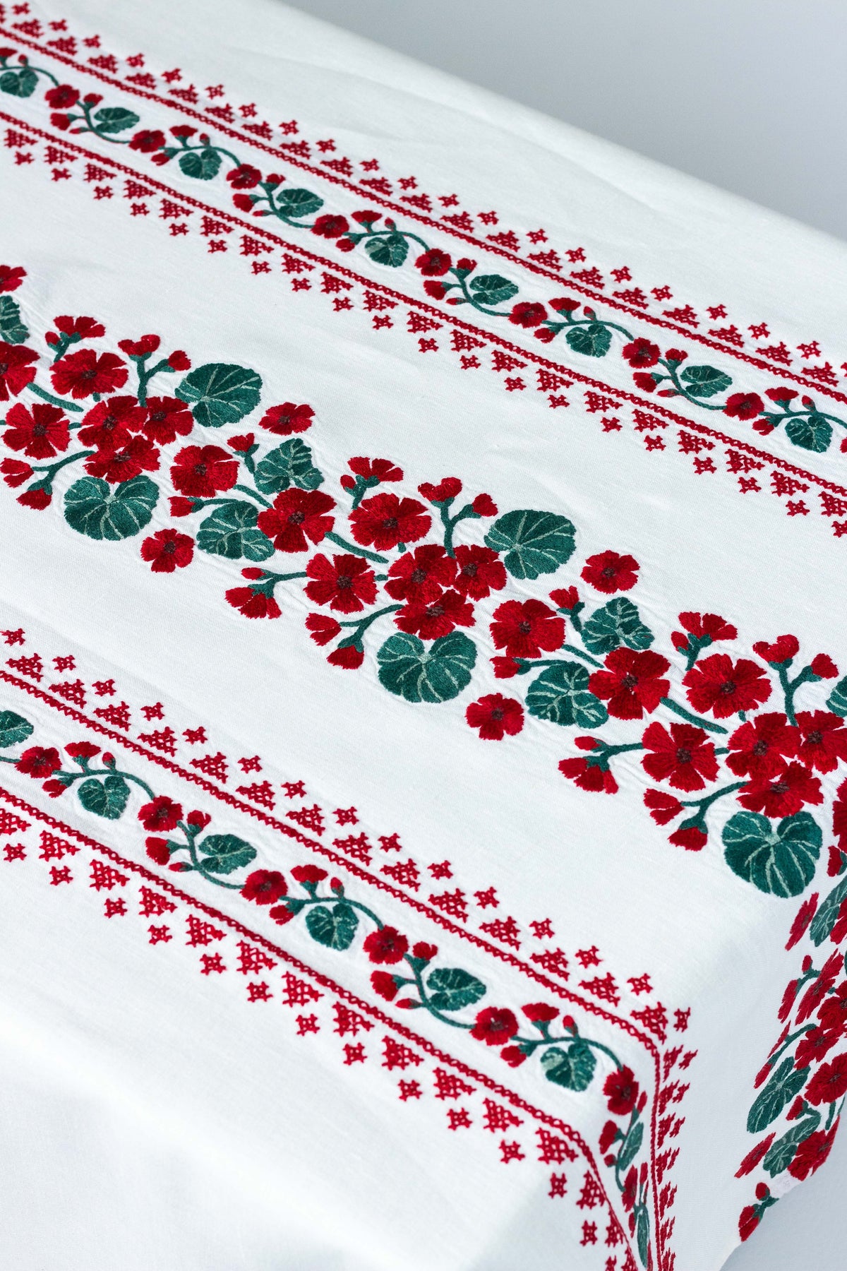 Detail view of Geranio rectangular tablecloth showcasing red embroidered geraniums and green leaves on white background