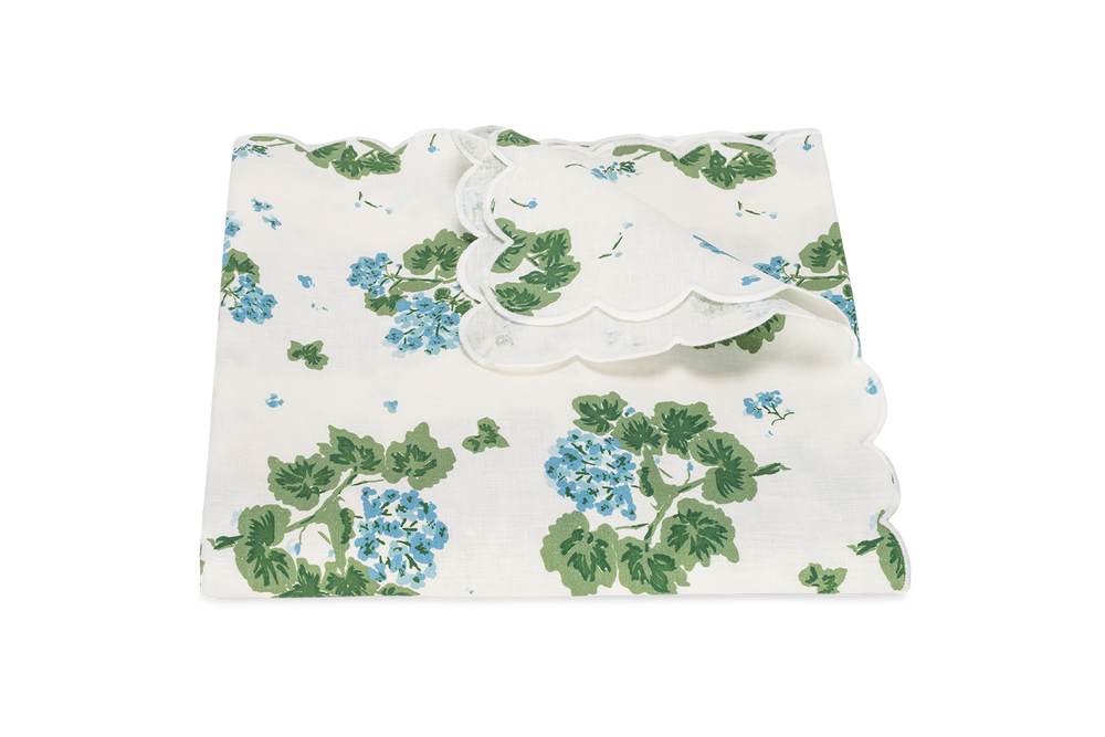 Folded Geranium tablecloth showing blue geranium floral print, scalloped edged hem, and linen texture on white background