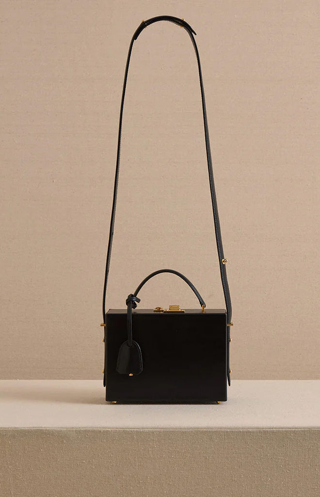 Front view of Grace 18 box bag in smooth black calf leather with top handle, long adjustable shoulder strap and gold hardware on beige background