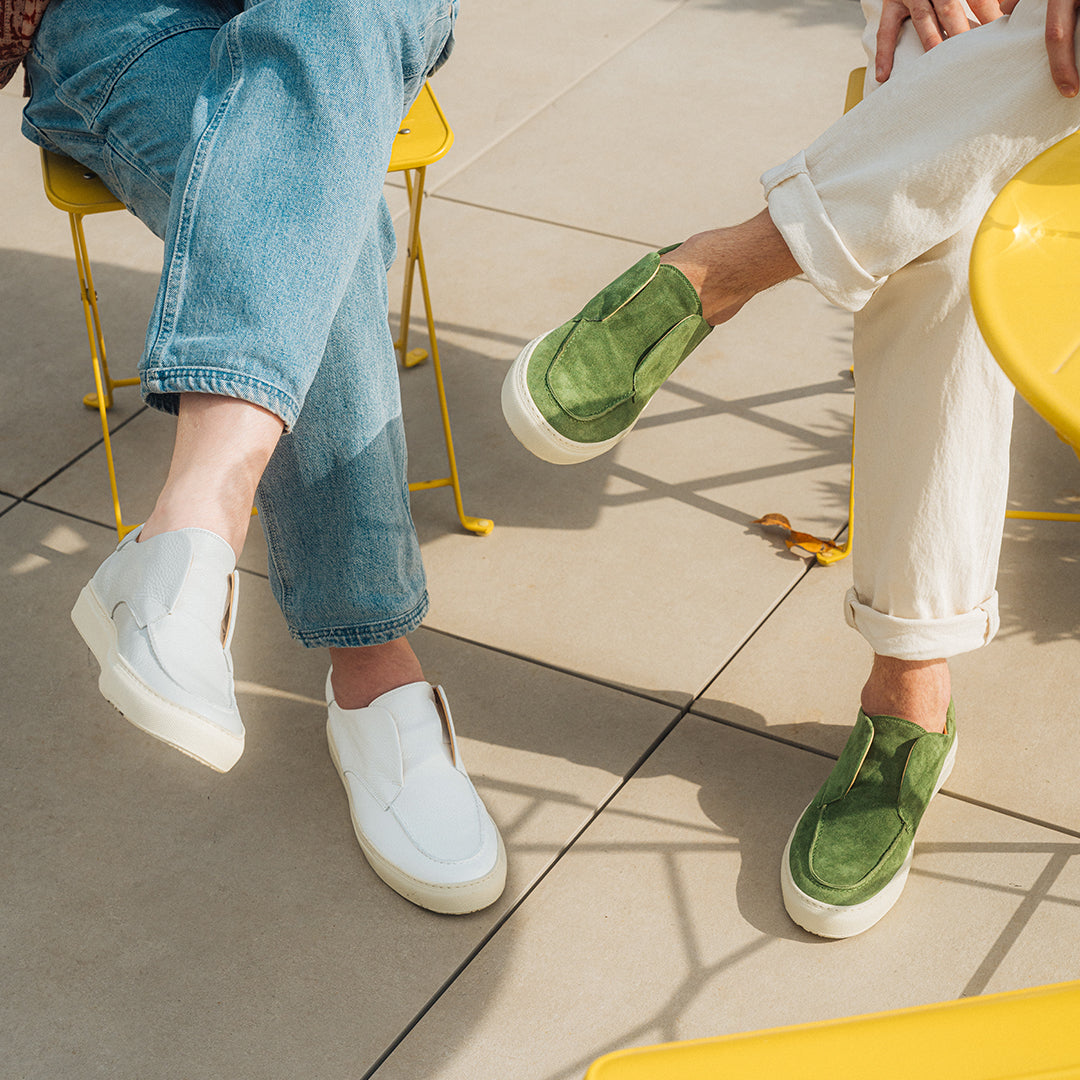 Side view of Men’s Green Suede Pitti Sneaker showcasing slip-on design and rubber sole with seated wearers on a tiled patio