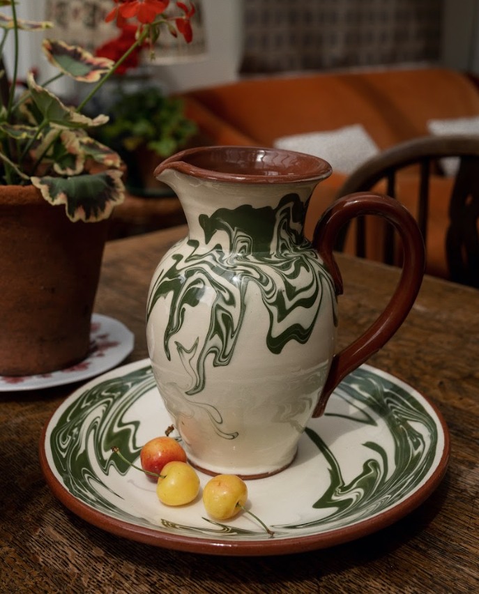 Angled view of Marbre jug showcasing green marbled ceramic pattern and brown handle on matching plate on wooden table