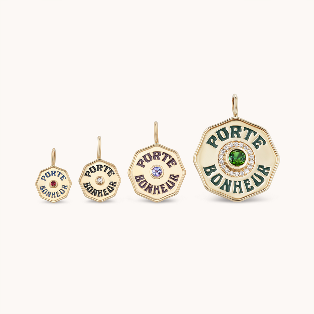Front view of four Wee PB charms in graduated sizes showing ‘Porte Bonheur’ inscription and white diamond centers on a cream background