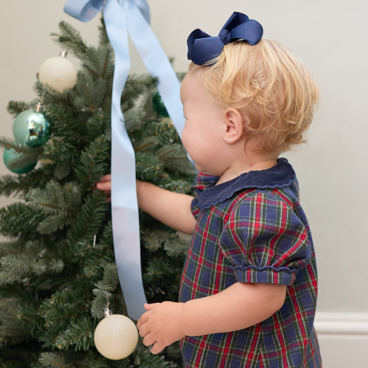 Child wearing the Beatrice Bubble in Tinsel Tartan while decorating a Christmas tree